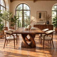 Rectangular dining table on a single pedestal of interlocking twisted ribbons in a bright dining room with arched windows and plants