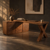 Corner detail of l shaped desk with an x leg and a cabinet with carved ripple fronts beside wood, brass and linen samples