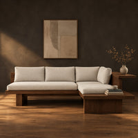 L shaped sofa with cream cushions on a low wood platform base in a dark studio against a charcoal plaster wall