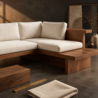 Corner detail of l shaped sofa with cream cushions on a low wood platform base beside wood, brass and linen samples