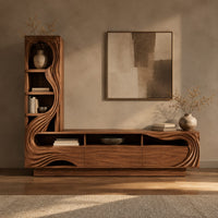 Corner detail of tv stand with a tall arched shelf tower and flowing carved lines beside wood, brass and linen samples