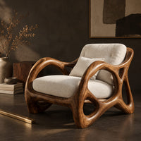 Corner detail of lounge chair with large loop openings in the arms and sculpted legs beside wood, brass and linen samples