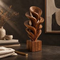 Corner detail of wood sculpture of layered swirling petals rising from a square block base beside wood, brass and linen samples