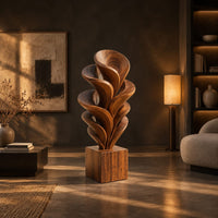 Wood sculpture of layered swirling petals rising from a square block base in a dark living room at golden hour