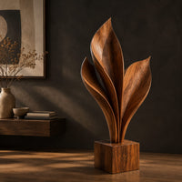 Wood sculpture of sweeping leaf blades rising from a square block base, three-quarter view showing the grain