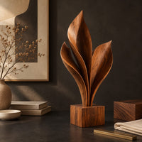 Corner detail of wood sculpture of sweeping leaf blades rising from a square block base beside wood, brass and linen samples