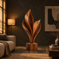 Wood sculpture of sweeping leaf blades rising from a square block base in a dark living room at golden hour