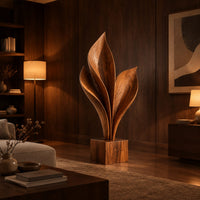 Wood sculpture of sweeping leaf blades rising from a square block base in an evening living room with walnut wall paneling