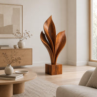 Wood sculpture of sweeping leaf blades rising from a square block base in a Scandinavian living room with white walls