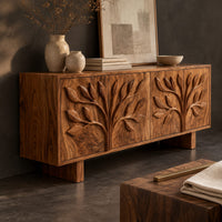 Corner detail of low sideboard carved with two leafy branch trees across four doors beside wood, brass and linen samples