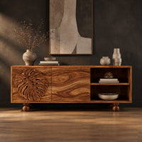 Sideboard with a carved leaf door, open shelf bay and ball feet in a dark studio against a charcoal plaster wall