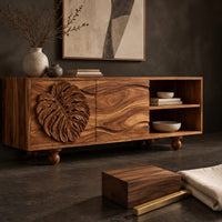 Corner detail of sideboard with a carved leaf door, open shelf bay and ball feet beside wood, brass and linen samples