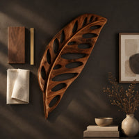 Detail of leaf shaped wooden wall sculpture with open oval cutouts and carved veins beside wood, brass and linen samples