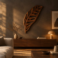 Leaf shaped wooden wall sculpture with open oval cutouts and carved veins above a low console in an evening living room