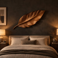 Leaf shaped wooden wall sculpture with raised carved veins and a curling stem above a bed in a dusk lit bedroom
