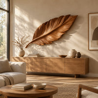 Leaf shaped wooden wall sculpture with raised carved veins and a curling stem above a light oak sideboard in daylight