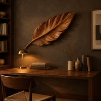 Leaf shaped wooden wall sculpture with raised carved veins and a curling stem above a desk in a dark study corner