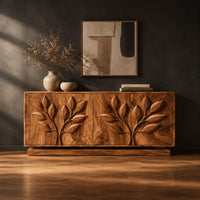 Sideboard with two carved leafy branches across four doors on a plinth in a dark studio against a charcoal plaster wall
