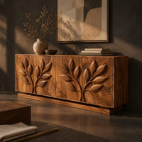 Corner detail of sideboard with two carved leafy branches across four doors on a plinth beside wood, brass and linen samples