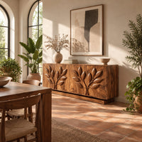 Sideboard with two carved leafy branches across four doors on a plinth in a bright dining room with arched windows and plants