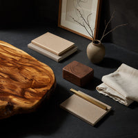 Corner detail of thick live edge slab coffee table on block pedestals beside wood, brass and linen samples