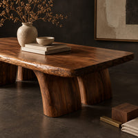 Corner detail of live edge coffee table with a thick slab top and four stout tapered legs beside wood, brass and linen samples
