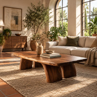Live edge coffee table with a thick slab top and four stout tapered legs in a bright living room with arched windows and plants