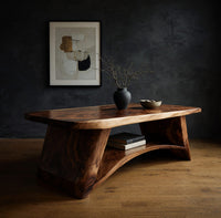 Live edge coffee table with sculpted legs and a low shelf in a dark studio against a charcoal wall