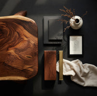 Corner detail of live edge coffee table with sculpted legs and a low shelf beside wood, brass and linen samples