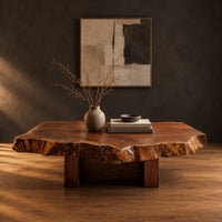 Live edge coffee table with a rugged slab top and block base in a dark studio against a charcoal plaster wall