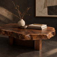 Corner detail of live edge coffee table with a rugged slab top and block base beside wood, brass and linen samples