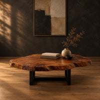 Live edge coffee table with a wide irregular slab top on a dark frame in a dark studio against a charcoal plaster wall