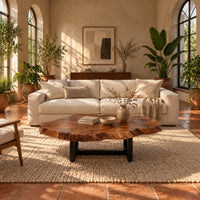 Live edge coffee table with a wide irregular slab top on a dark frame in a bright living room with arched windows and plants