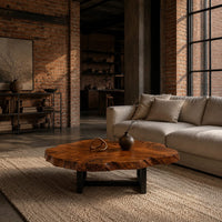 Live edge coffee table with a wide irregular slab top on a dark frame in an industrial loft living room with exposed brick