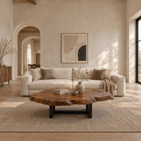 Live edge coffee table with a wide irregular slab top on a dark frame in a bright open plan living room