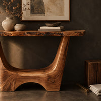 Corner detail of live edge console table with a u shaped base and a low arched foot beside wood, brass and linen samples