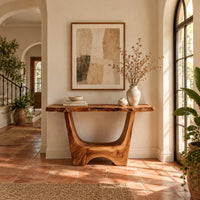 Live edge console table with a u shaped base and a low arched foot in a bright entryway with arched windows and plants