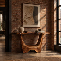 Live edge console table with a u shaped base and a low arched foot in an industrial loft entryway with exposed brick