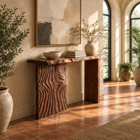 Live edge console table with a carved ripple slab leg in a bright entryway with arched windows and plants