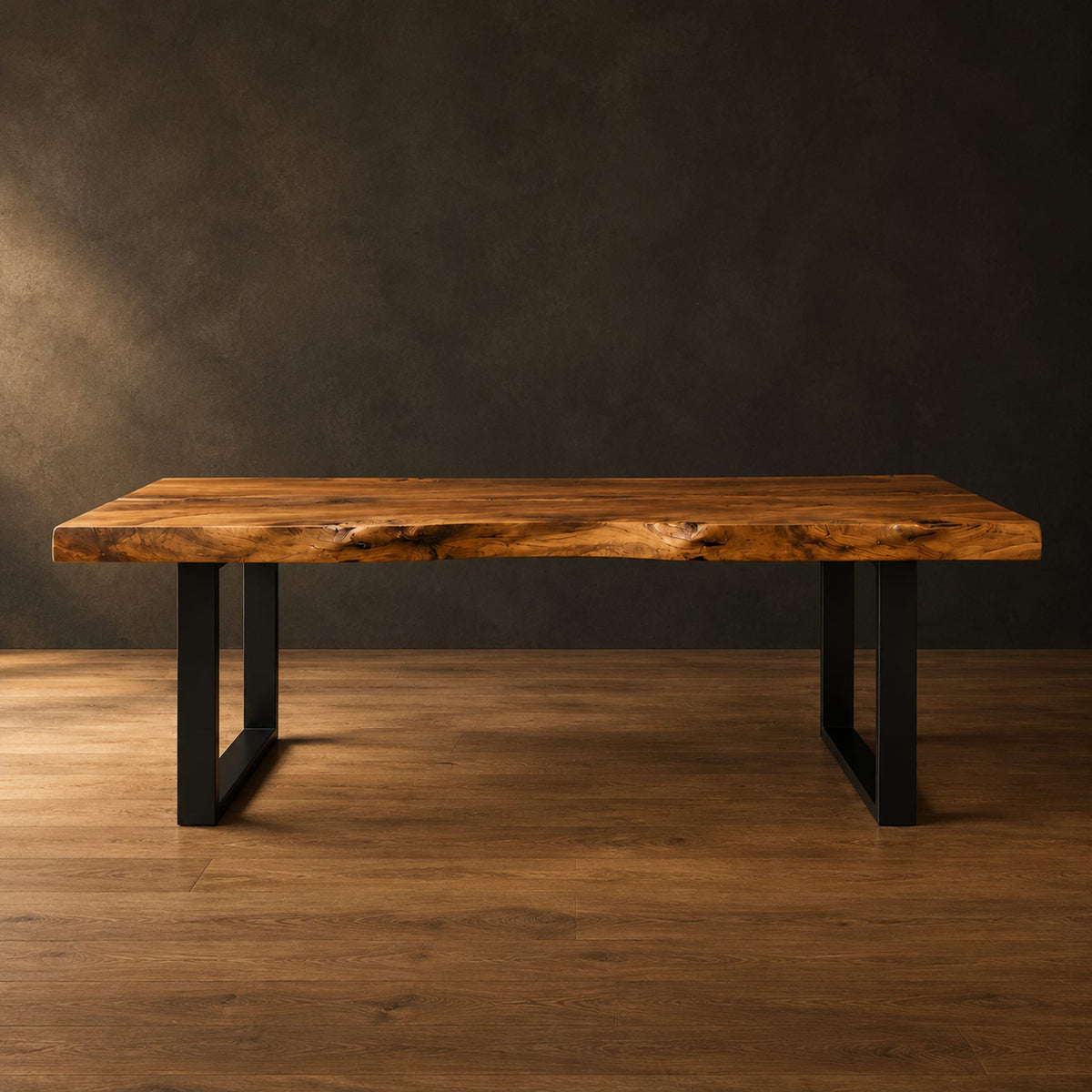 Live edge wooden desk with a thick slab top and black u shaped legs in a dark studio against a charcoal plaster wall