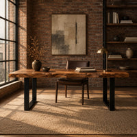 Live edge wooden desk with a thick slab top and black u shaped legs in an industrial loft home office with exposed brick