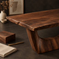 Corner detail of live edge dining table on two sculpted arch pedestals beside wood, brass and linen samples