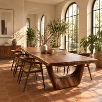 Live edge dining table on two sculpted arch pedestals in a bright dining room with arched windows and plants