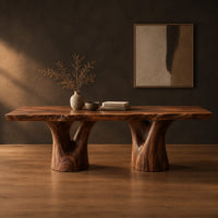 Live edge dining table on two forked trunk pedestals in a dark studio against a charcoal plaster wall