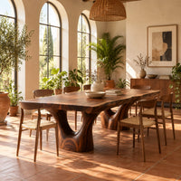 Live edge dining table on two forked trunk pedestals in a bright dining room with arched windows and plants