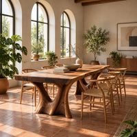 Live edge dining table on two sculpted trunk pedestals in a bright dining room with arched windows and plants