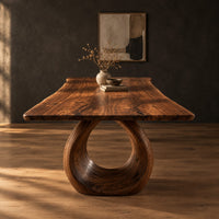 Live edge dining table on a large open ring pedestal base in a dark studio against a charcoal plaster wall