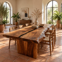 Live edge dining table with a dark center seam and a slab base in a bright dining room with arched windows and plants