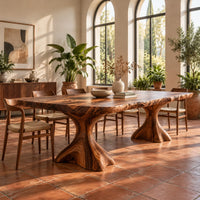 Live edge dining table with a figured top on two flared root pedestals in a bright dining room with arched windows and plants