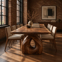 Live edge dining table on a single sculpted pedestal with a teardrop opening in an industrial loft dining room with exposed brick
